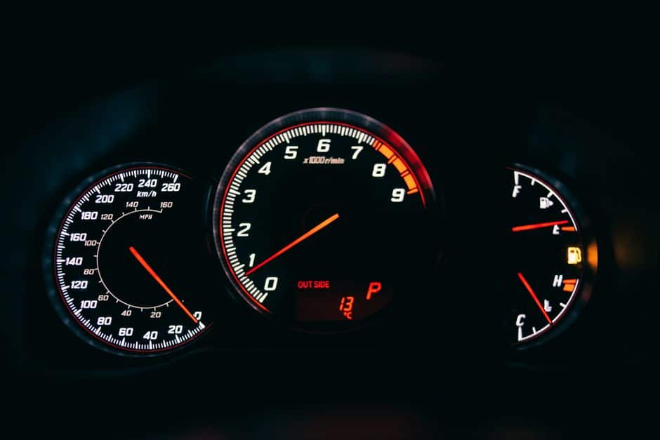 Tachometer between speedometer and fuel gauge with arrows and scales in car on black background
