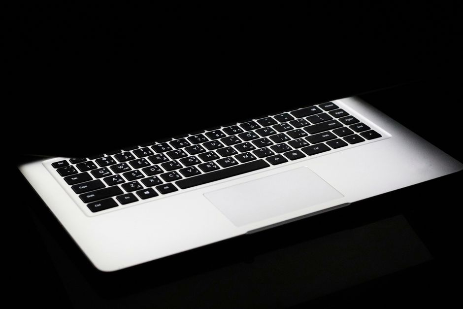 A modern laptop with a glowing keyboard illuminated in a dark, minimalist setting.