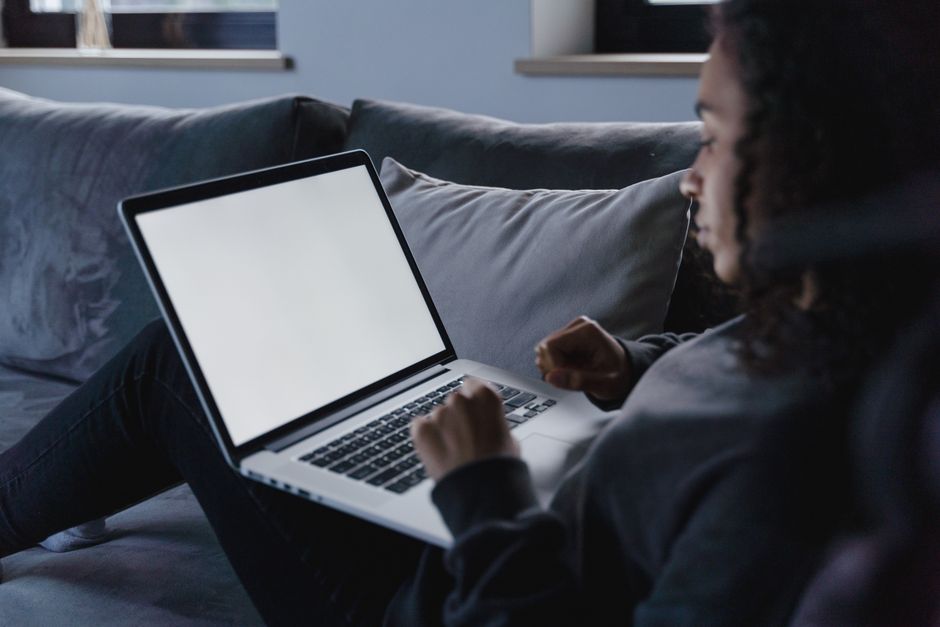 A young woman works on her laptop in a cozy living room, focusing on the blank screen.