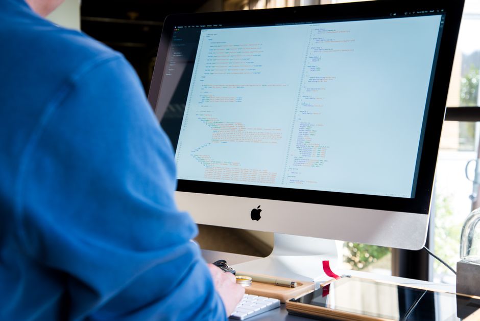 A programmer in a blue shirt coding on an iMac. Perfect for technology or work-related themes.